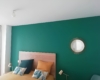 Belle chambre verte aux contraste lumineux avec un petit bien agencé avec des coussins assortie au lit et mur.